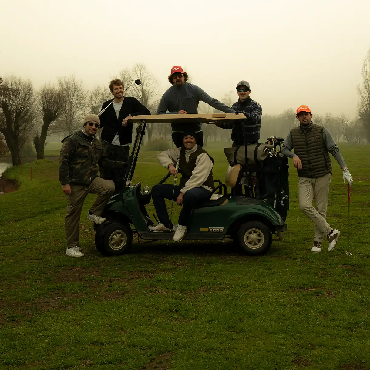 Group of men in sportswear around a golf cart on a golf course.