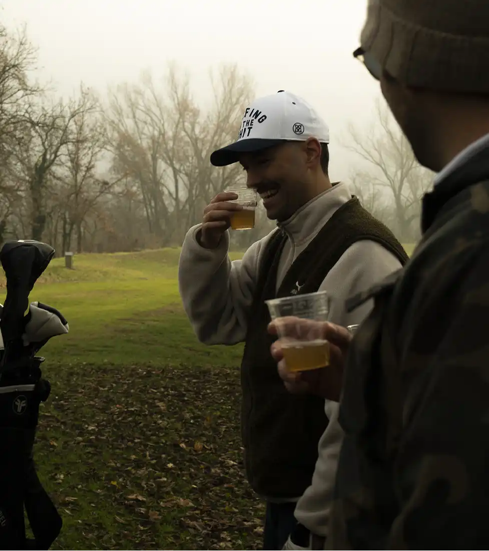 Two smiling men drinking a beverage on a golf course in autumn.